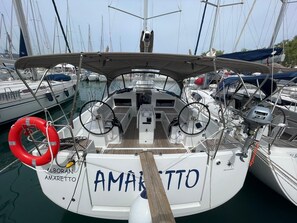 Un barco llamado 'AMARETTO' atracado en un puerto deportivo con otros barcos, un timón y un flotador salvavidas.