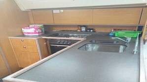 A compact kitchen with a gas stove, a sink, and wooden cabinets. - Sun-Kissed Sailing Journey in Trat, Koh Chang (Ko Chang)