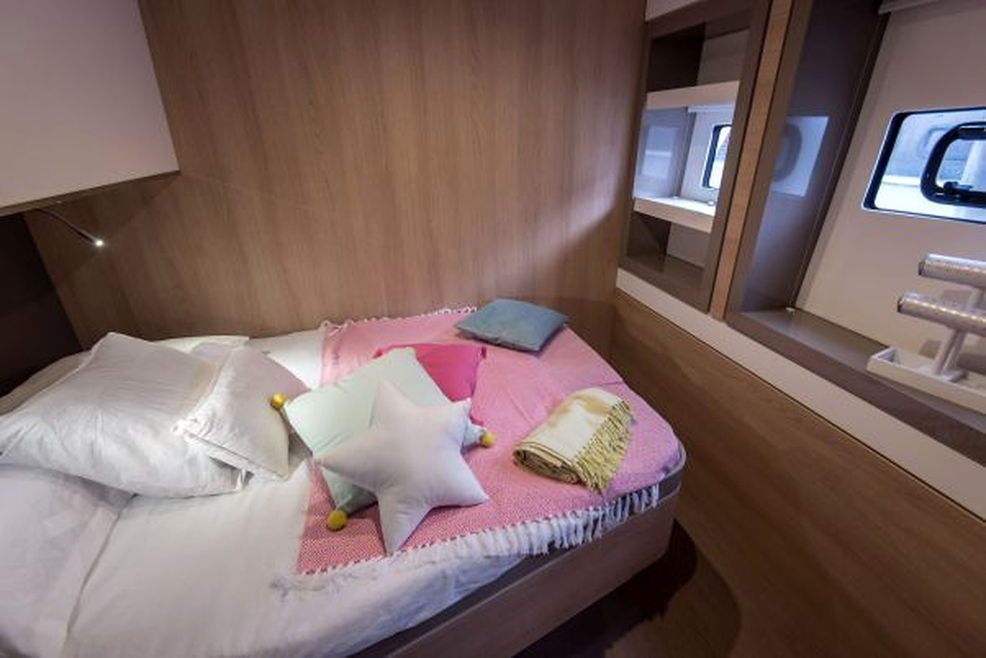 A neatly made bed with pillows and a blanket, a bedside table with a lamp, and a window with a view.