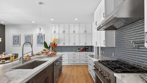 Une cuisine moderne avec des meubles blancs, un plan de travail en marbre, une cuisinière à gaz et un plancher en bois.