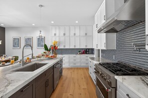 A modern kitchen with white cabinets, a marble countertop, a gas stove, and a wooden floor.