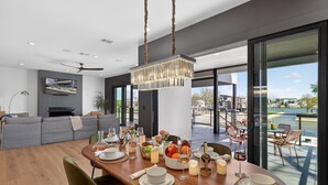Un espace de repas moderne avec une table en bois dressée pour le repas, un grand lustre et une vue sur l’extérieur.