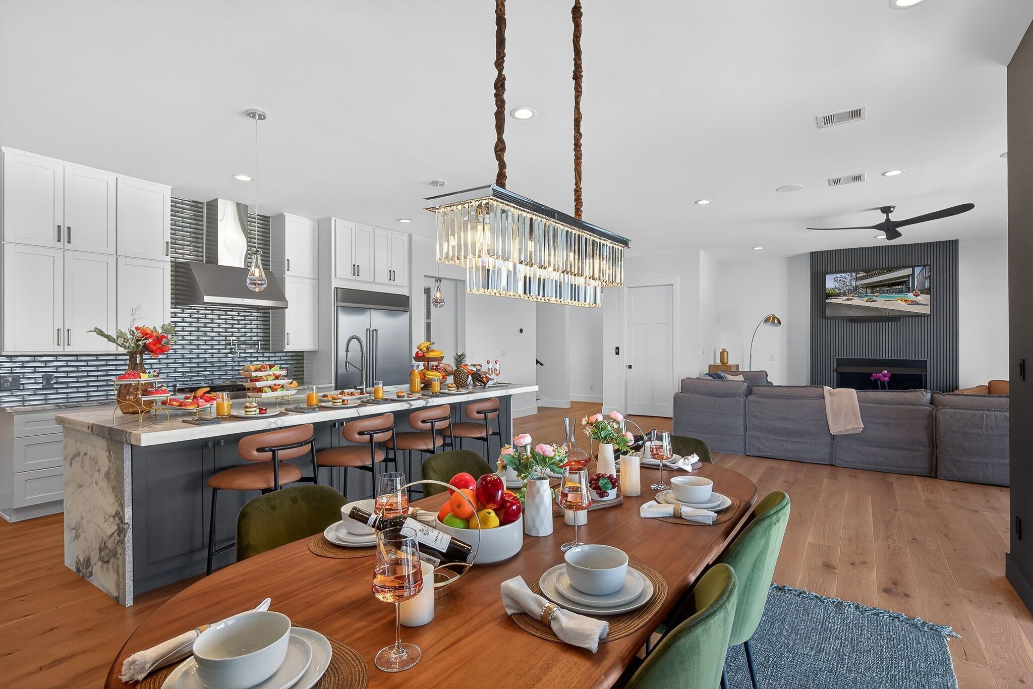 Une cuisine moderne dotée d’un îlot central, un coin repas avec une table en bois mise pour le repas, et un espace de vie avec un canapé et un téléviseur.