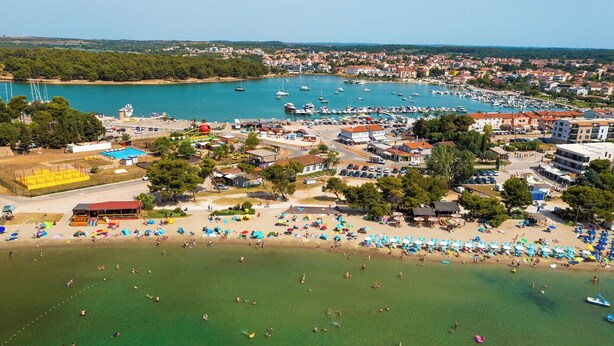 Luftaufnahme einer Küstenstadt mit einem Yachthafen, Strand und verschiedenen Gebäuden.