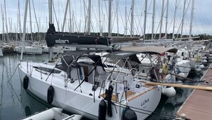 Una marina con varios veleros amarrados, una embarcación más pequeña al frente y un muelle de madera.