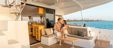 Interior de un yate con zona de comedor, sofá y vista al mar.