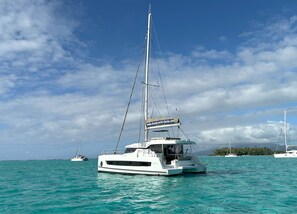 A sailboat with a website banner on the deck, surrounded by calm turquoise waters and other boats in the distance.