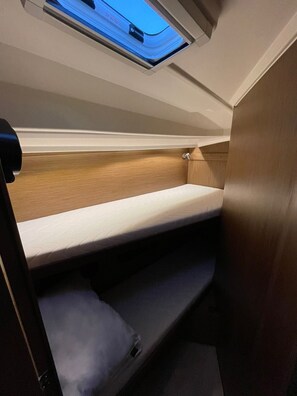 A bunk bed with a skylight above, wooden paneling, and a mattress with a patterned cover.