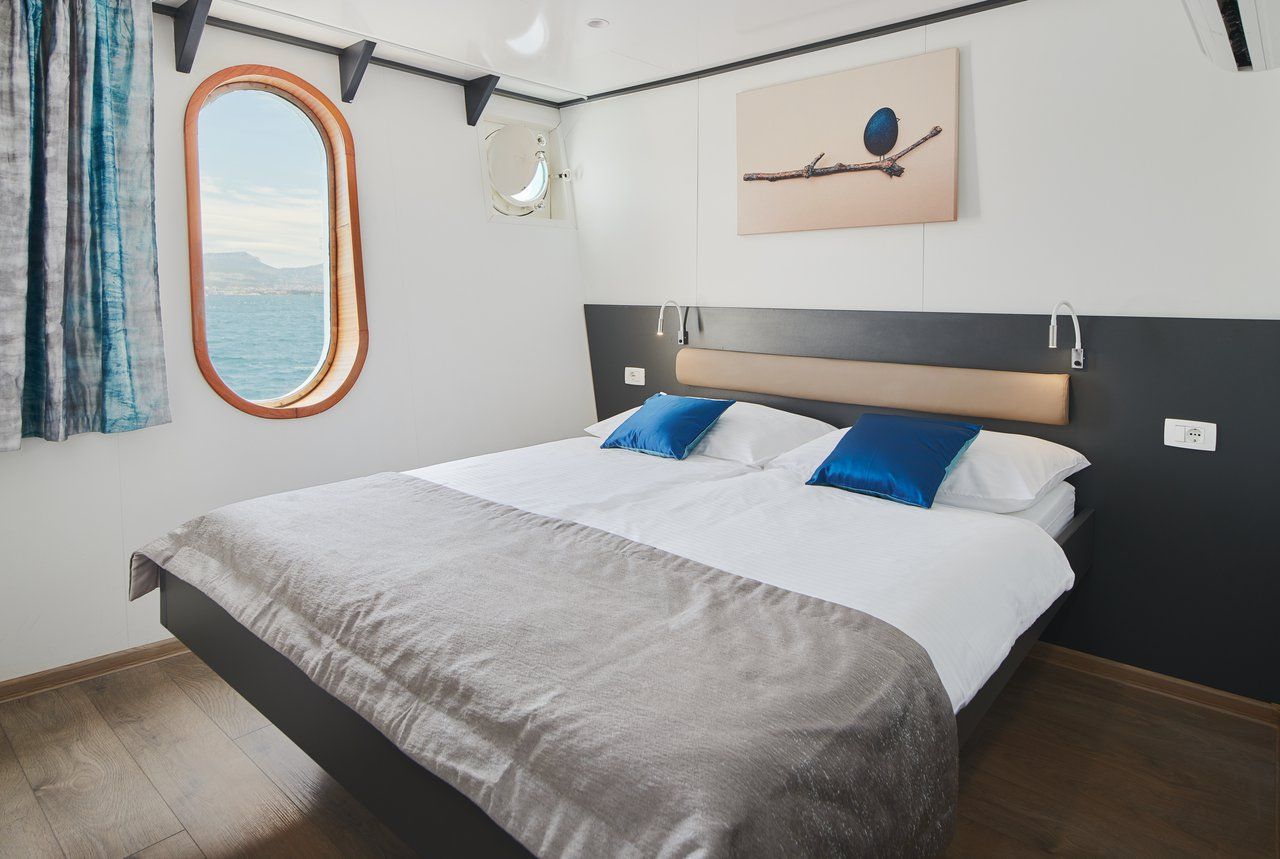 A modern hotel room with a large bed, a window with a view, a headboard, and a wall-mounted artwork.