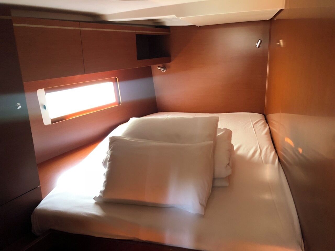 A compact, single-bed room with a window, wooden walls, and a small shelf.