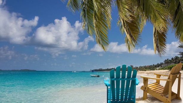 A beach scene with clear turquoise water, a boat in the distance, and two wooden chairs. - Caribbean Bliss: Sun-soaked Sailing Adventure from Nassau, Bahamas (Nassau)