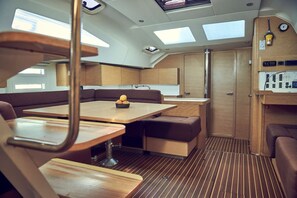 A compact kitchen with wooden cabinets, a dining area with a table and benches, and a control panel on the right. - Sun-Kissed Sailing Adventure in Istria, Croatia (Pula)