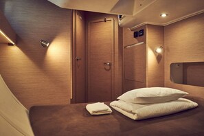 A compact, well-lit room with a wooden finish, a bed with pillows and a folded towel, a door, and a small window. - Sun-Kissed Sailing Adventure in Istria, Croatia (Pula)