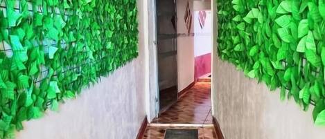 A hallway with green artificial foliage on the walls, a wooden patterned floor, and a sign reading 'BIENVENIDO' at the end.