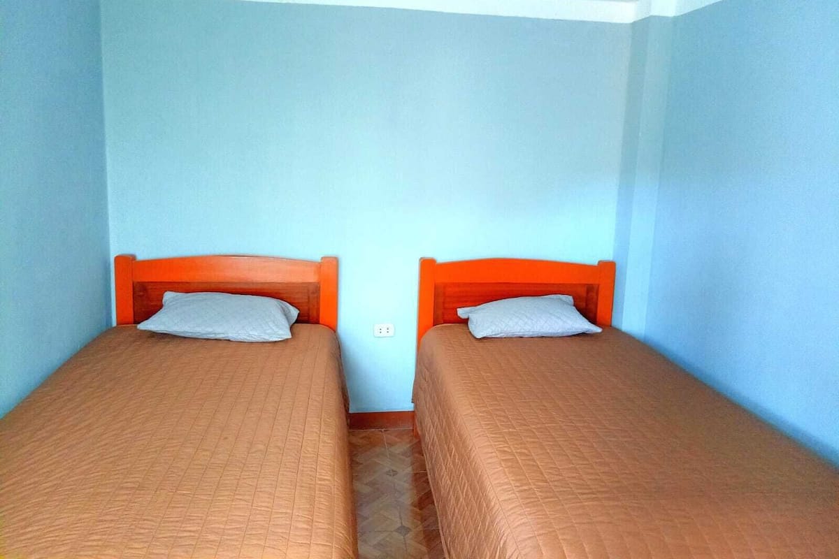 Una habitación con dos camas individuales, cada una con cabecera de madera y un almohadón.