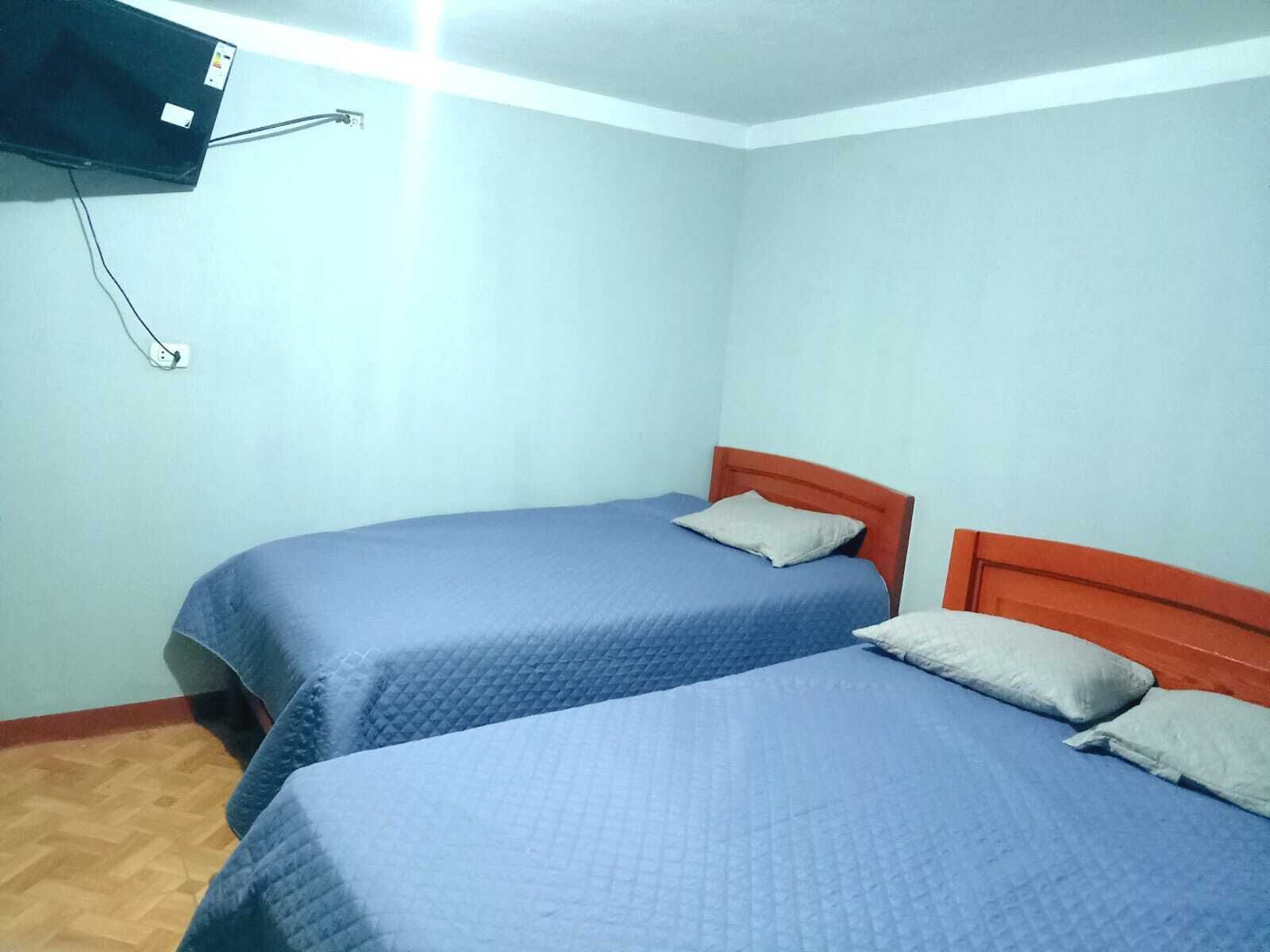 Een kamer met twee bedden, een aan de muur bevestigde televisie en een houten vloer.