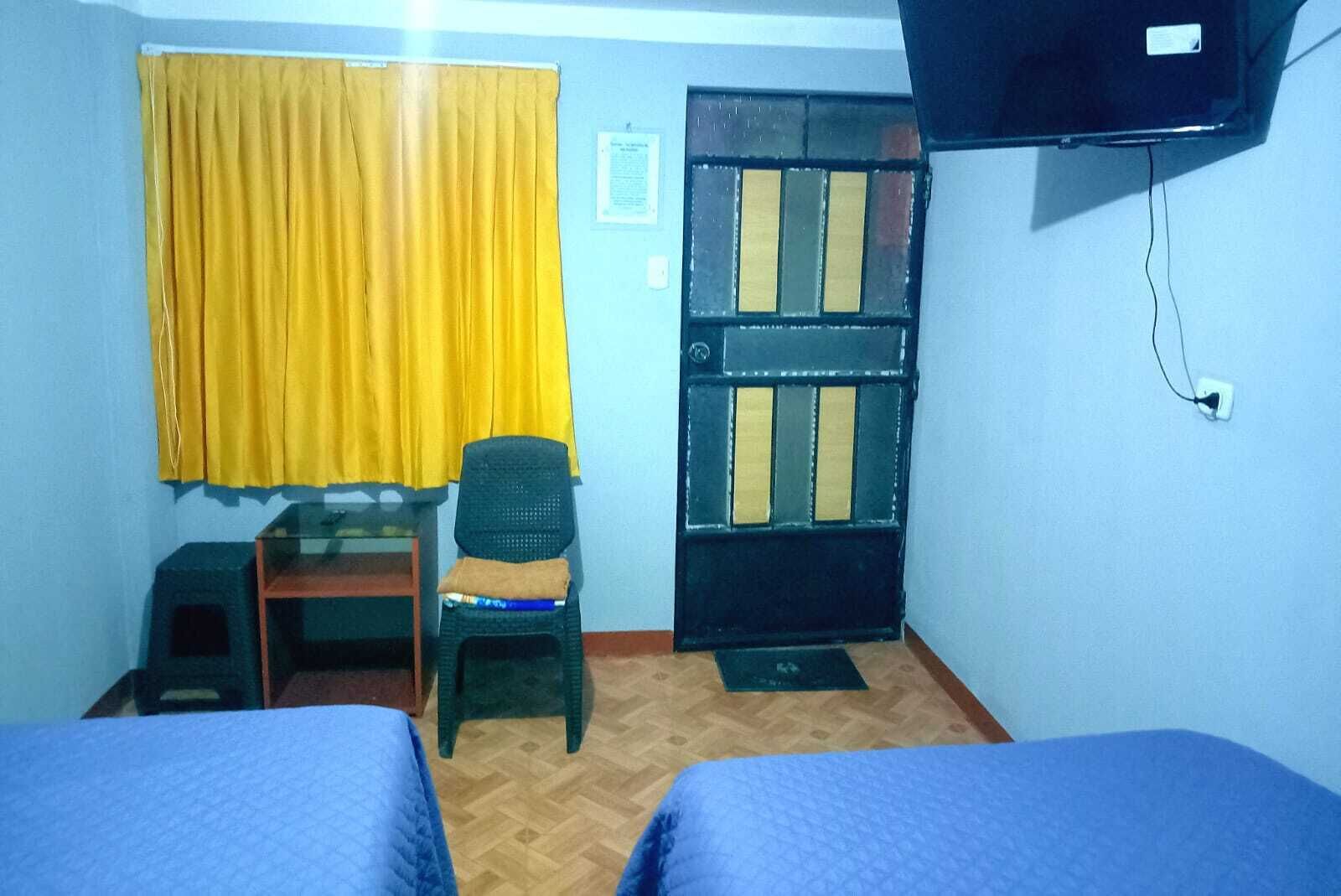 Une chambre avec deux lits, un bureau, une chaise, un téléviseur et une porte à motifs rayés.