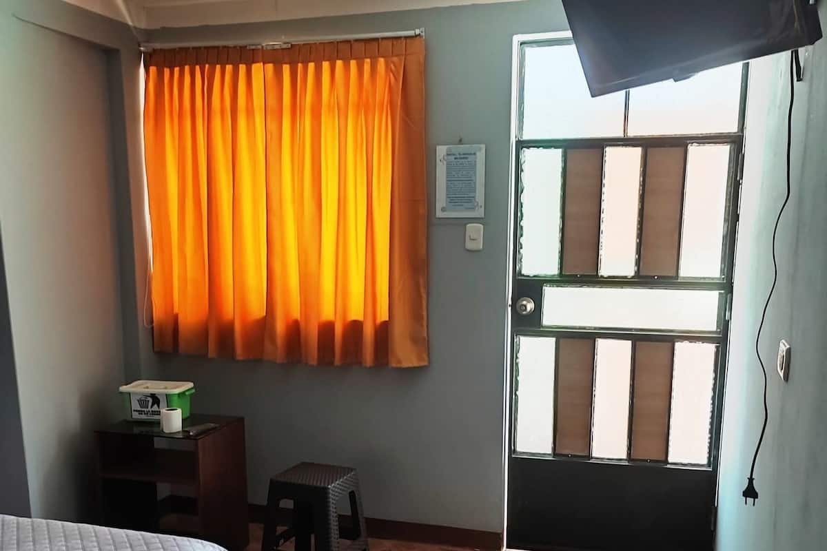 Una habitación con cama, escritorio, silla, ventana con cortinas y puerta.
