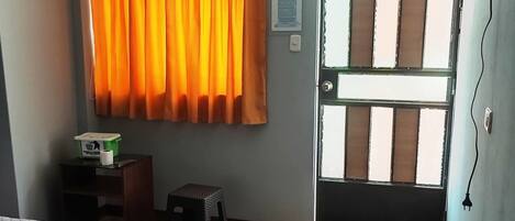 Una habitación con cama, escritorio, silla, ventana con cortinas y puerta.