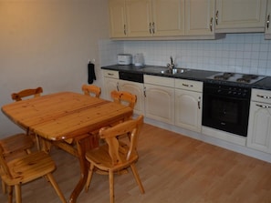 A kitchen with a wooden table and chairs, a dishwasher, a stove, and white cabinets.