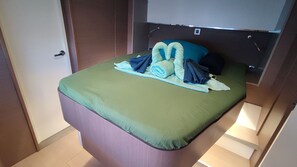 A compact bed with a green mattress, neatly folded towels, and a blue pillow.