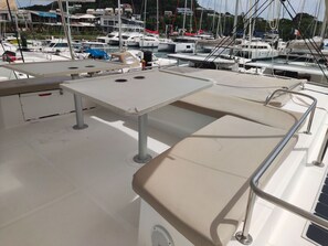 A boat deck with a table, cushioned seating, and a railing.