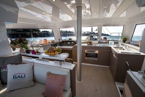 A yacht interior with a dining area, kitchen, and seating with a view of the sea.