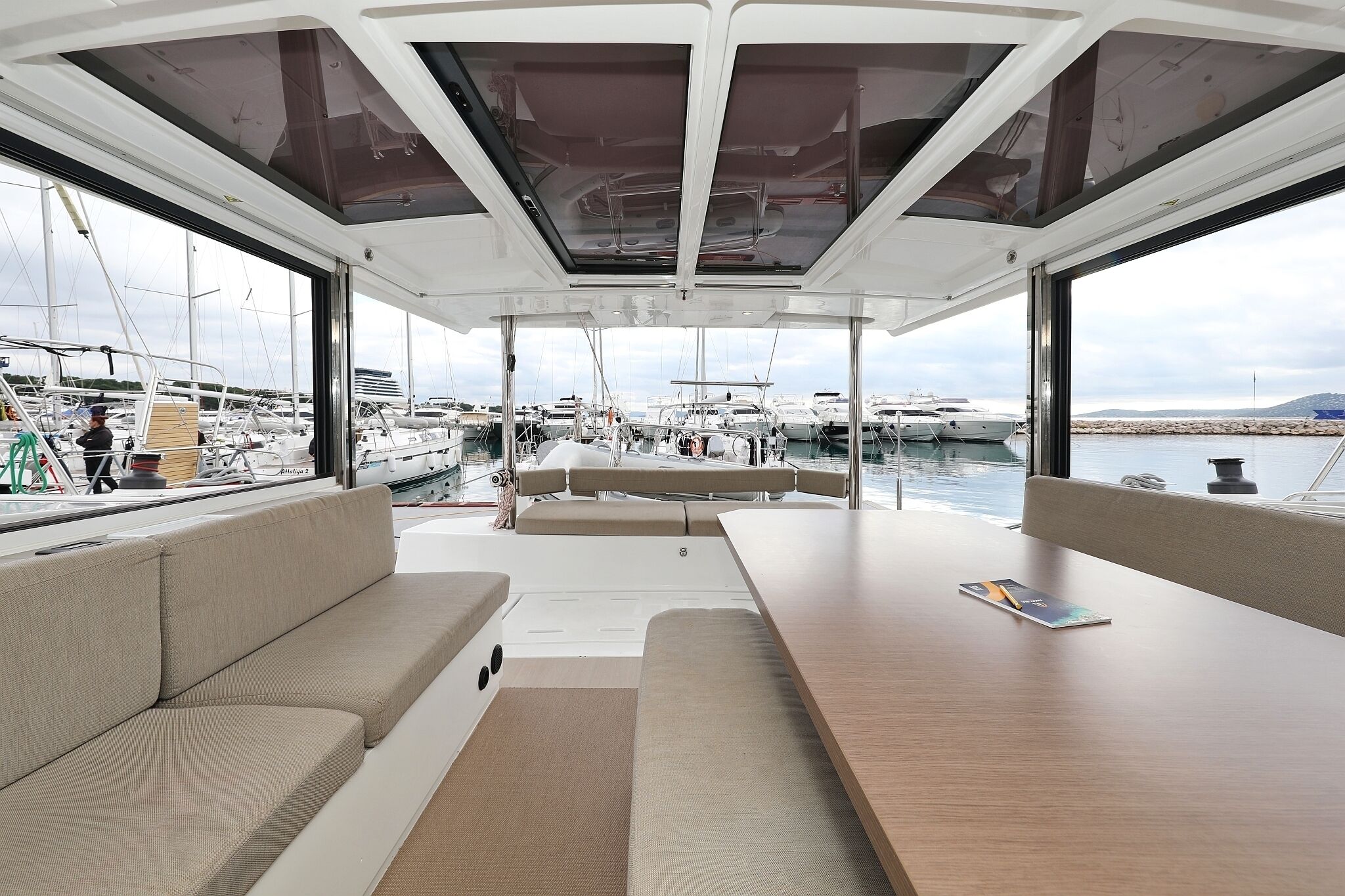 A yacht interior with a dining area, cushioned seating, and a view of the marina.