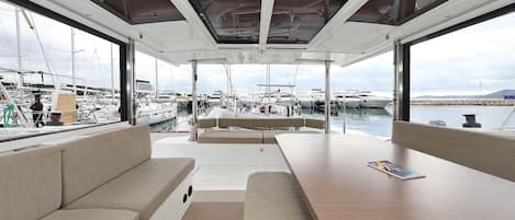 A yacht interior with a dining area, cushioned seating, and a view of the marina.