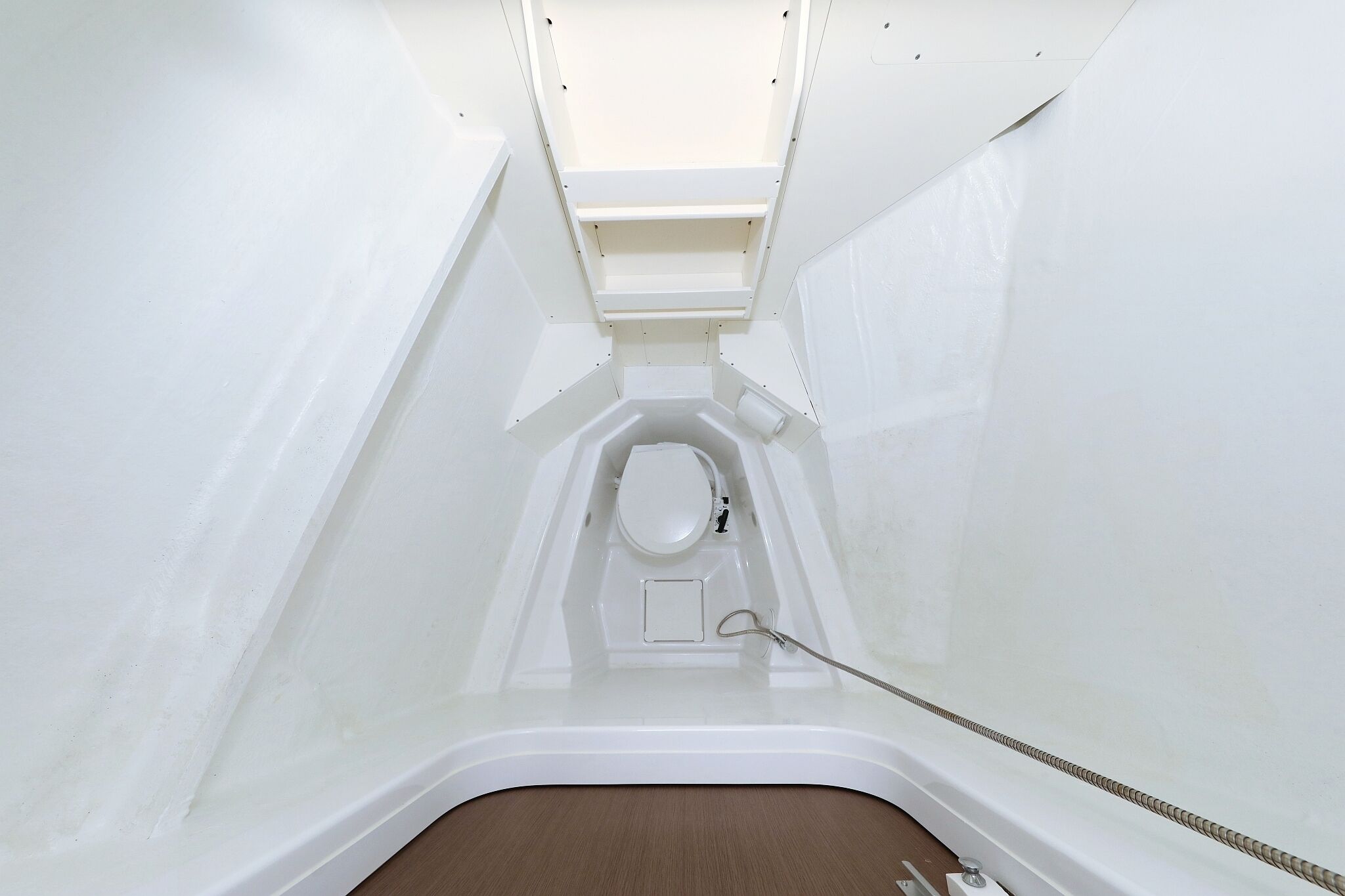 A compact, white, enclosed bathroom with a toilet, a small shelf, and a shower area.