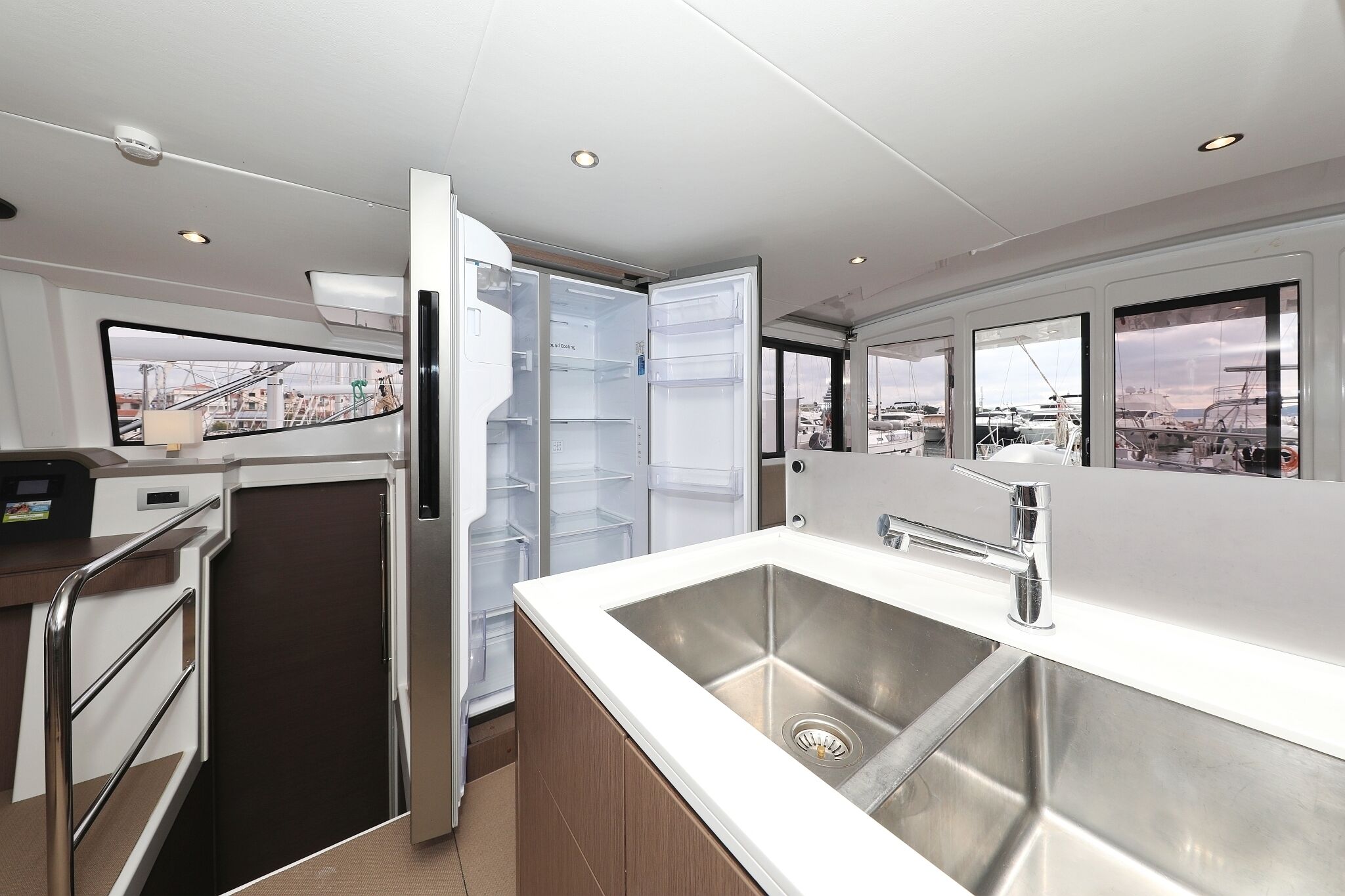 A modern kitchen with a stainless steel sink, a built-in refrigerator, and a view of the marina through the windows.