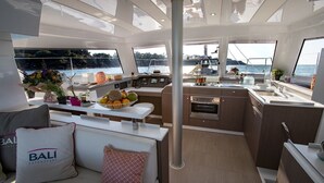 Interior de iate com área de jantar, cozinha e espaço de estar com vista para o mar.
