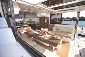Interieur van een jacht met een eetgedeelte, keuken en zithoek met uitzicht op het water.