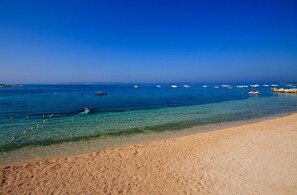 Uma praia com águas cristalinas, areia dourada e barcos ao longe.
