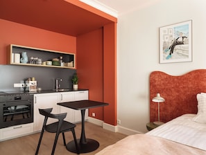 Ein gemütlicher Raum mit Küchenzeile, Essbereich, Bett und einem Bild an der Wand.