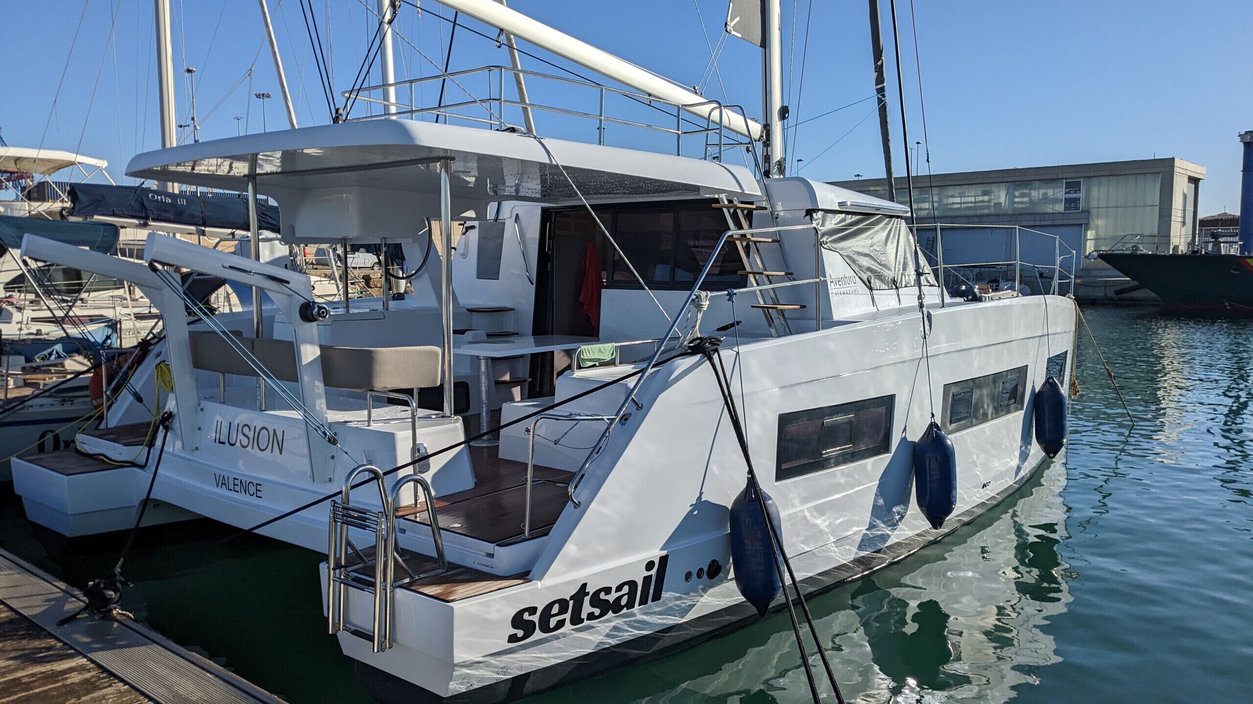Een witte jacht genaamd 'ILUSION' ligt afgemeerd in een jachthaven met 'setsail' branding, met een overdekt dek en een woongedeelte.