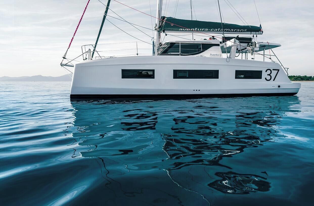 Un yate blanco con el número 37 en su lateral, llamado 'aventura-catamarans', flotando sobre aguas tranquilas.
