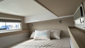 A compact, well-lit room with a bed, a window with a view of boats, and a small bedside table.