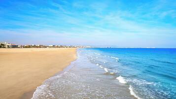 Une plage avec un ciel dégagé, un rivage sablonneux et des bâtiments en arrière-plan.