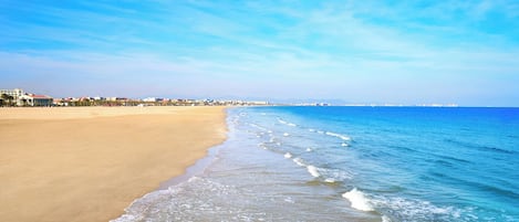 Una playa con cielo despejado, orilla arenosa y edificios al fondo.
