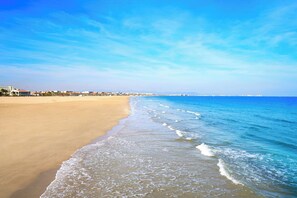 Una playa con cielo despejado, orilla arenosa y edificios al fondo.