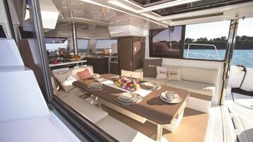 Interior de un yate con comedor, cocina y zona de estar con vista al agua.