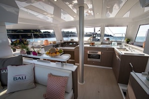 A yacht interior with a dining area, kitchen, and seating with a view of the sea.