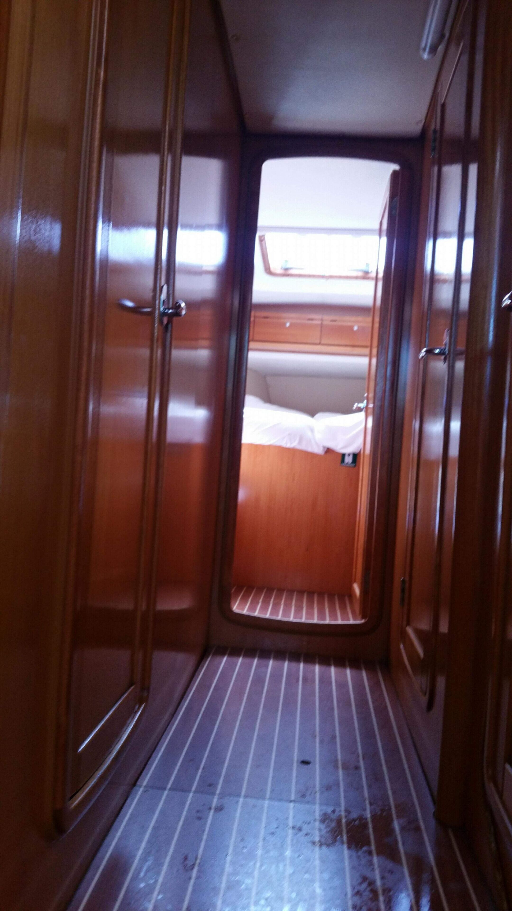 A narrow corridor with wooden doors leading to a cabin area with a bed and a window.