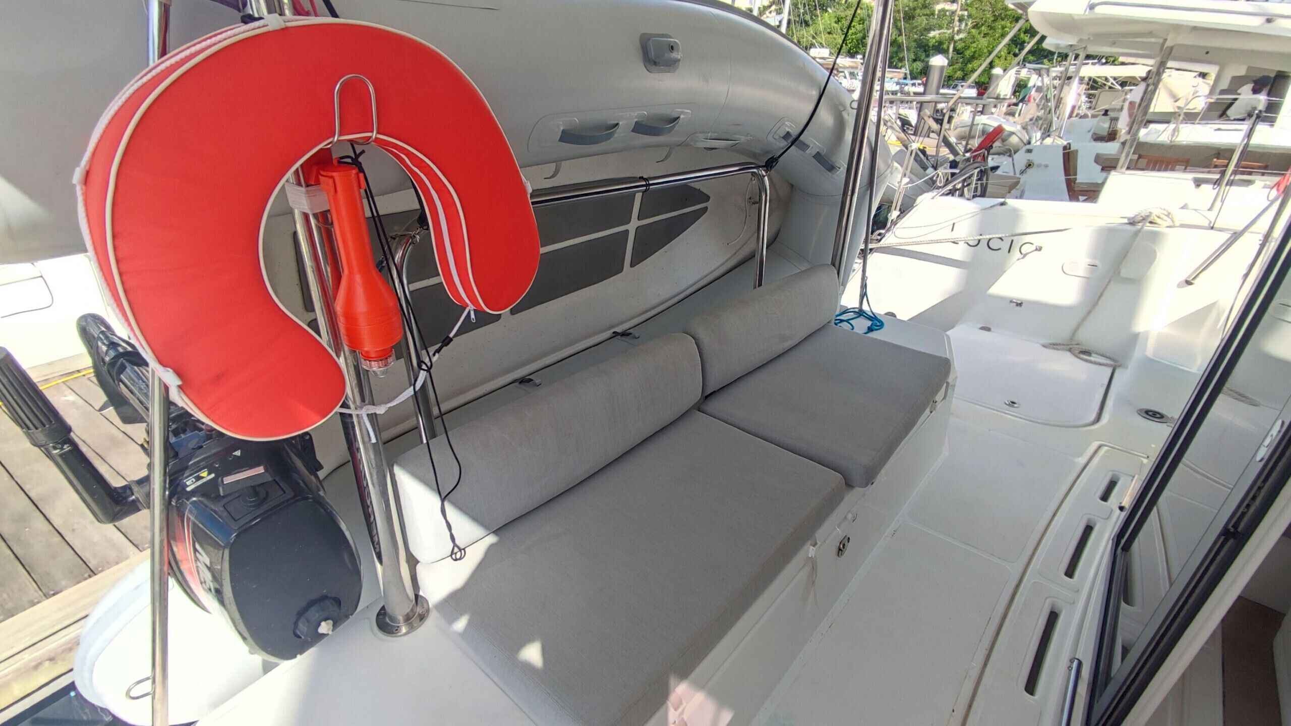 A boat's interior with a cushioned seating area, a red life ring, and a metal railing.
