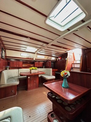 A boat interior with wooden paneling, a dining area, cushioned seating, and a small table with a vase of flowers. - Sun-Kissed Sailing Adventure in Islas Sarónicas (Alimos)