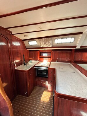 A compact galley with wooden cabinetry, a sink, and a stove. - Sun-Kissed Sailing Adventure in Islas Sarónicas (Alimos)
