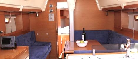 Un intérieur de bateau compact comprenant un coin repas, un petit espace salon et un panneau de commande.