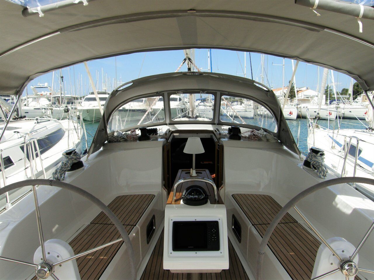 A boat's deck with a steering wheel, a central console, and a view of other boats in the marina.