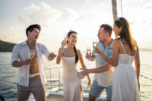 A group of people on a boat, holding glasses, with a body of water and a distant shoreline in the background.
